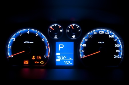 Illuminated car dashboard with dials, gauges and figures.