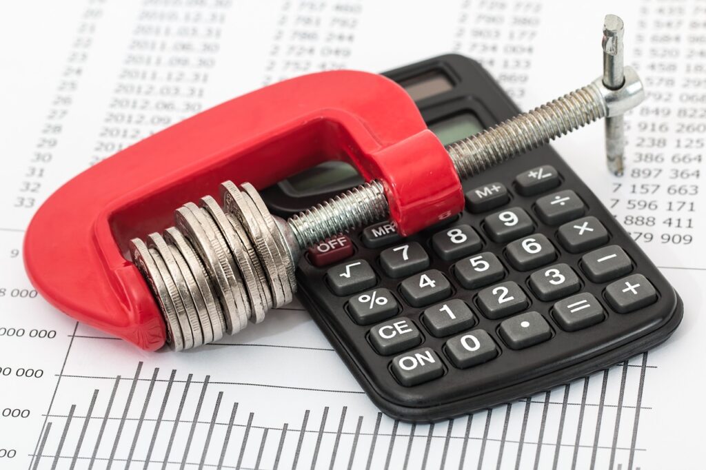 Are you feeling the squeeze? - A stack of coins held in a clamp on a calculator and business report