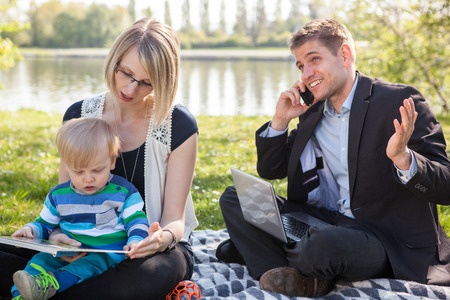 Three signs you’re addicted to work - a father is talking business on his phone while at a picnic with his young family