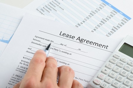 Lease or buy? - close-up of person hand with pen and calculator over lease agreement