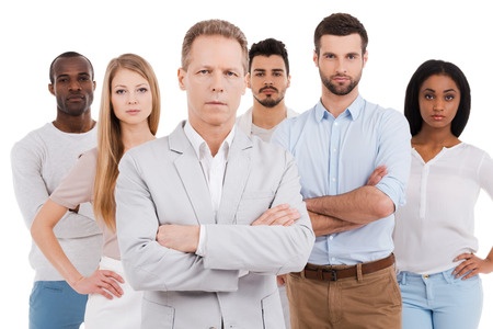 leading people to success. confident mature man in smart casual wear keeping arms crossed and looking at camera while group of young people standing behind him and against white background