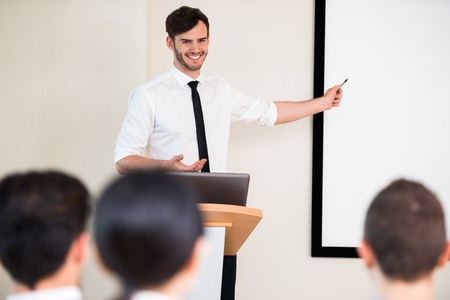 handsome young businessman making presentation with whiteboard on seminar or meeting to business people