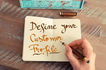 Profiling your customers - retro effect and toned image of a hand writing a note with a fountain pen on a notebook. handwritten text: define your customer profile