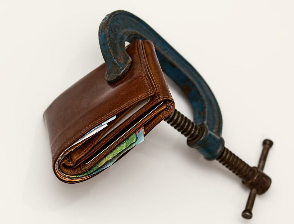 Small business strategies in a cost of living crisis - a wallet being squeezed in a clamp