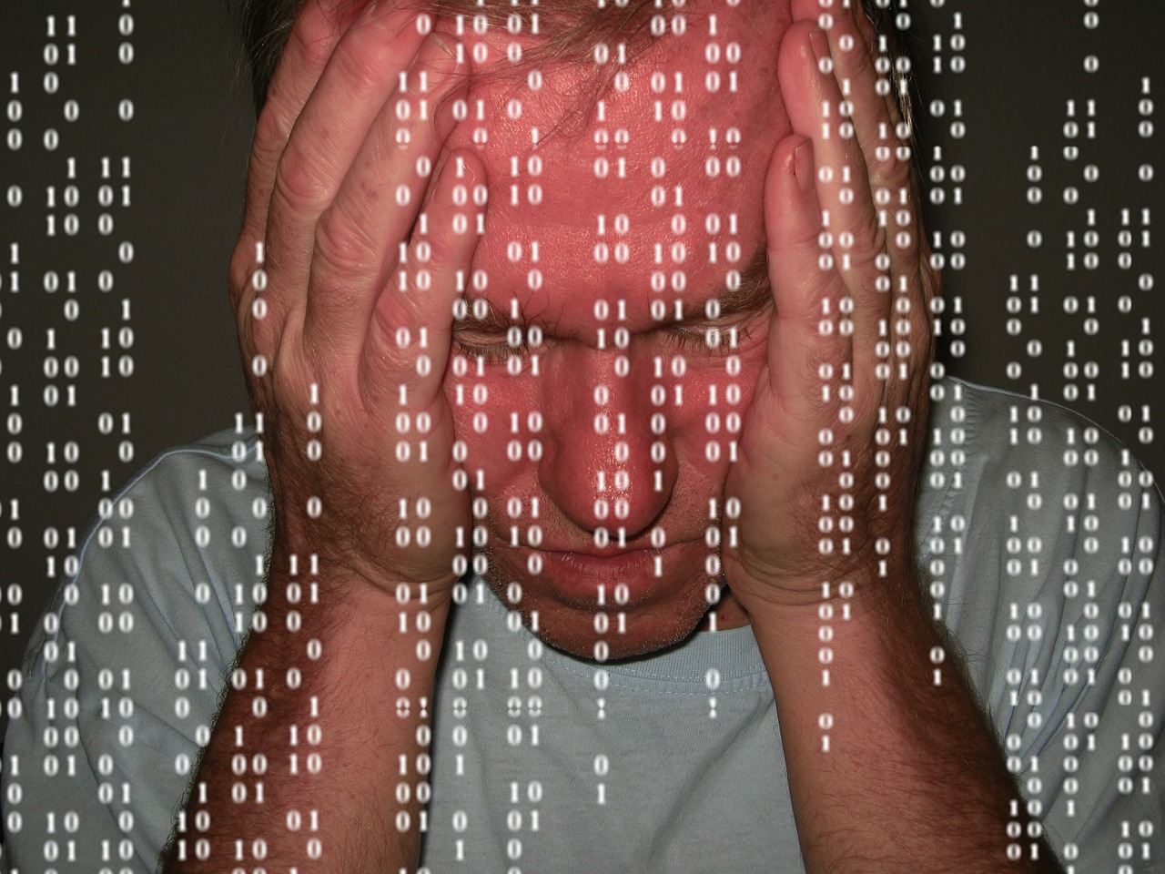 Tips for maintaining business data security - a man holds his head in his hands behind a screen of symbolic computer data