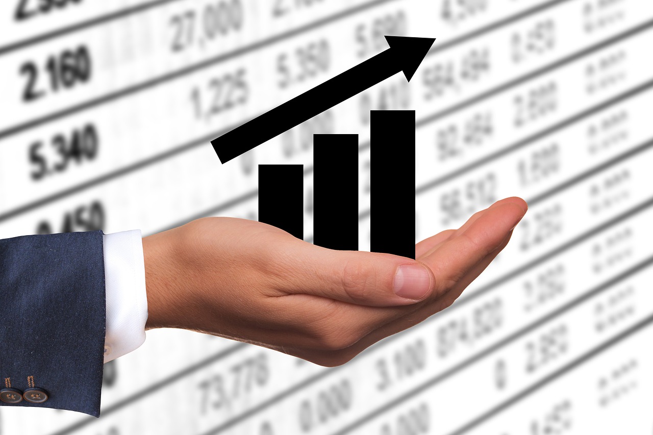 Business Update – 14 April 2022 - A hand holding an upward-trending bar chart, with a background of financial statistics