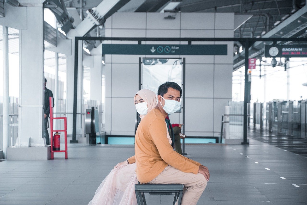 Covid-19 Business Update - 24 December 2020 - a man and a woman in face masks sit in a vitually deserted train station.