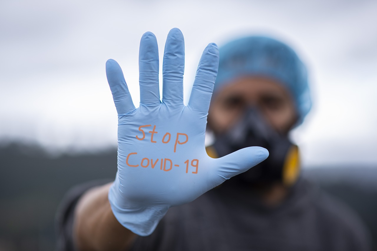 Pandemic preparedness tips for your business - a man in mask and surgical gloves and cap holds up a hand with the words "Stop Covid-19"