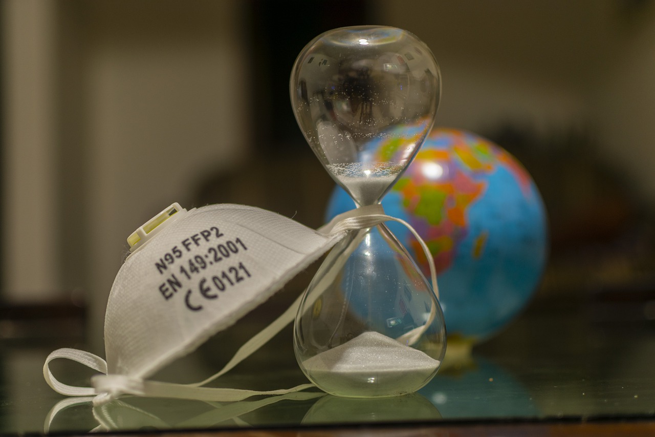 Business Update – 17 June 2021 - a face mask and an hourglass in front of a globe map. Waiting for travel restrictions to lift.