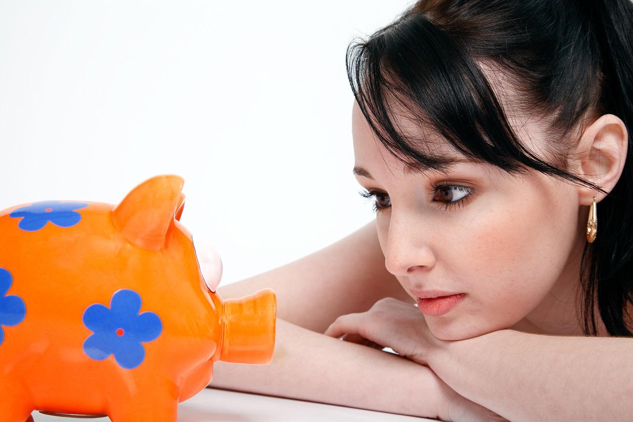 How to Choose the Right Savings Account for You - a woman gazes thoughtfully at a piggy bank